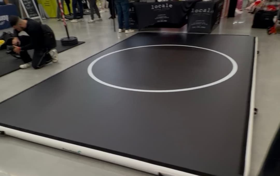 A 10 by 16 Pro FlowMat laid out on the floor of a busy expo hall, with vendor stands and a crowd behind it