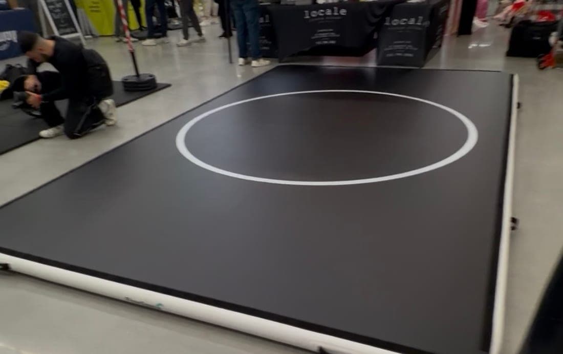 A 10 by 16 Pro FlowMat laid out on the floor of a busy expo hall, with vendor stands and a crowd behind it